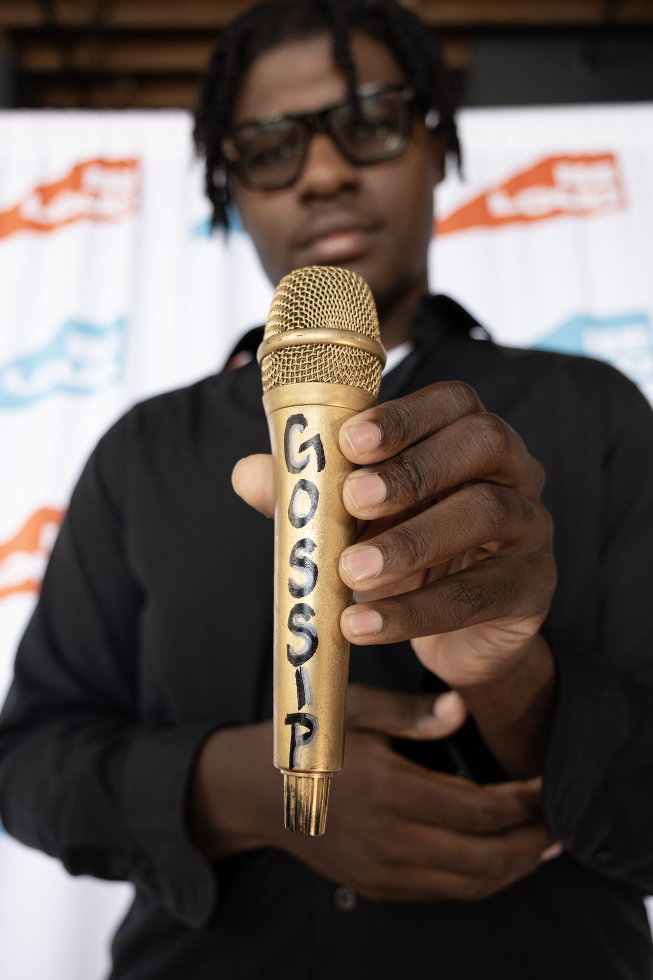 A young host holding up a gold microphone labeled Gossip
